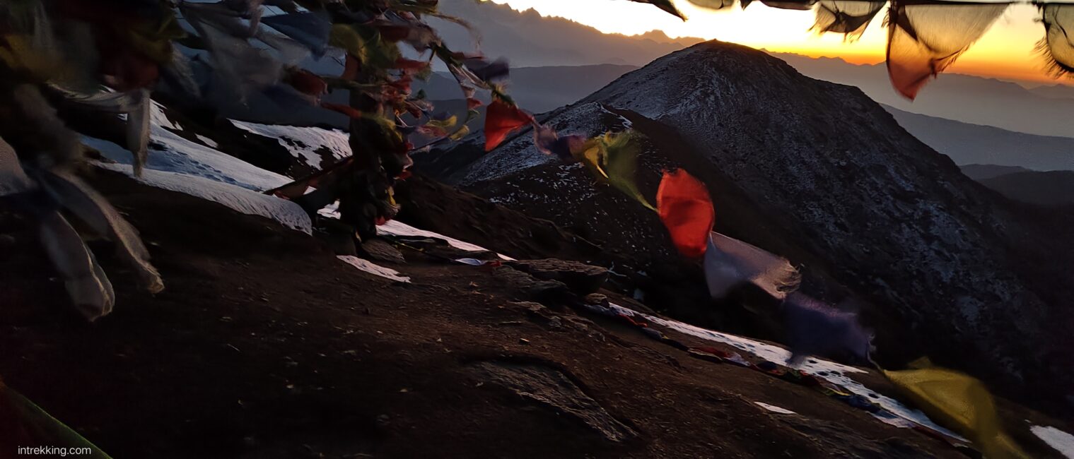 Prayer flags blowing in the wind on a mountainside at sunset.