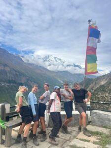 Group of trekkers posing with a local guide against mountain backdrop and prayer flags.