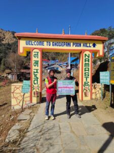A trekking guide and client at the entrance gate of Ghorepani Poonhill holding the company sign hoarding board 
