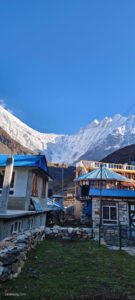 Guest houses with blue roof in a mountain village with snow-capped mountain backdrop 